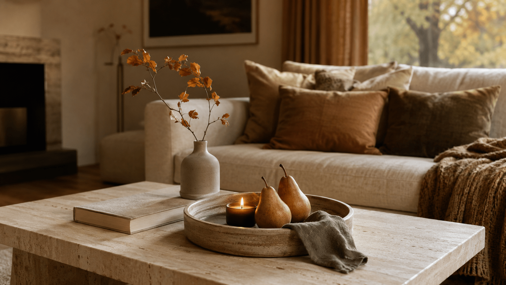 Herbstlich dekorierter kleiner Couchtisch mit starkem Centerpiece aus runder Keramikschale, zwei Birnen, kleiner Kerze, Leinentuch, geschlossenem Buch und schmaler Vase mit Herbstzweig vor einem gemütlichen Sofa.